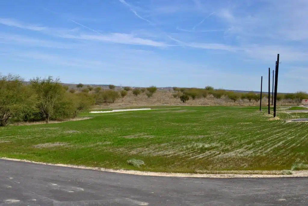 a large grassy field with a road in the foreground