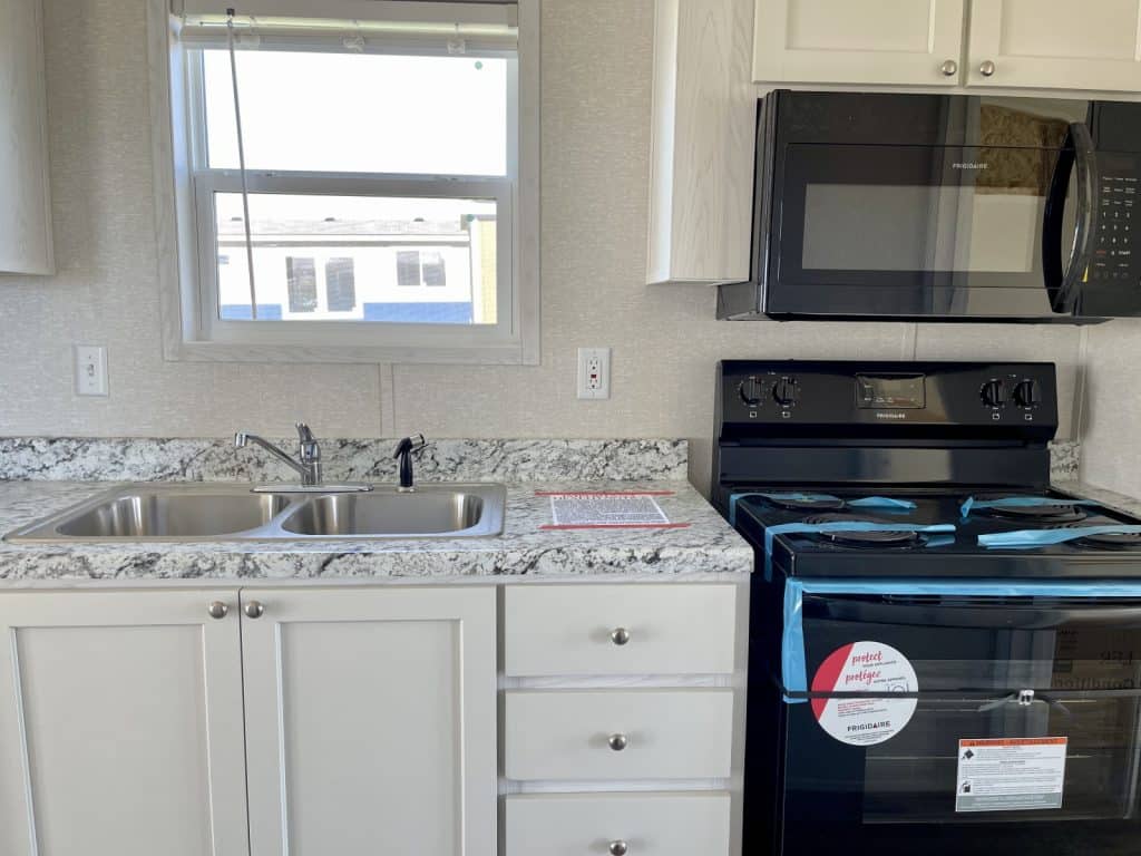 beautiful tiny mobile home kitchen with white cabinet and window with sink and stove